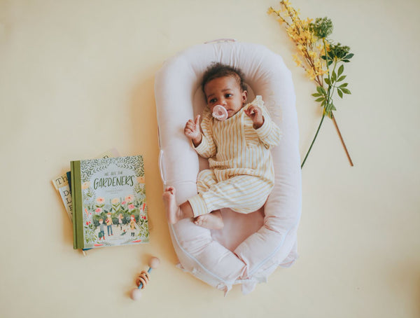 Little girl lying in a DockATot Deluxe+ dock with flowers and books around her