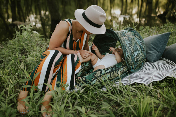 woman sitting in a grassy woodland with her baby lounging in a DockATot Deluxe+ with Cabana Kit