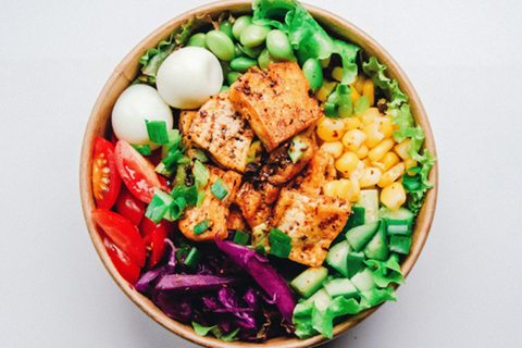 colorful bowl of high protein foods including salmon, hard boiled eggs, edamame, corn and tomatoes