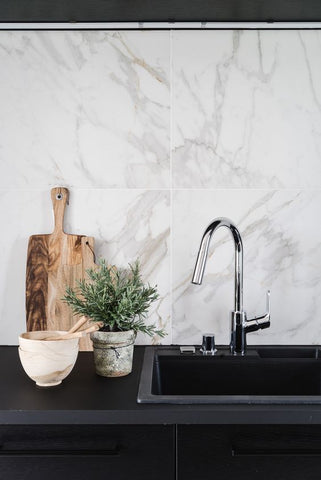 Black benchtop with sink chrome tap, wooden chopping boards and marble tile splashback