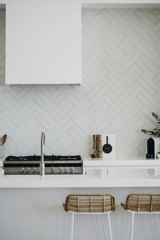 White kitchen stove top, rangehood and herringbone tile splashback