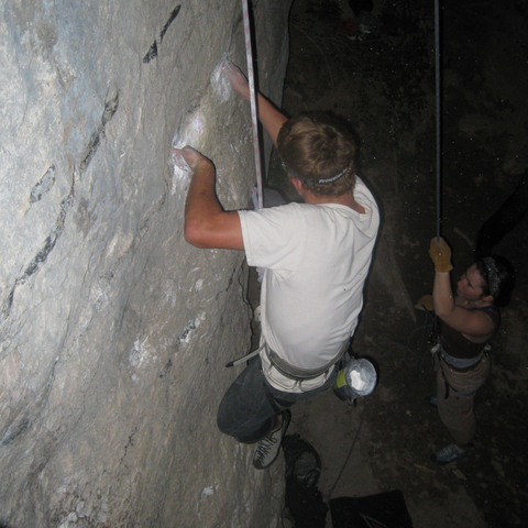 woman belaying a man climbing a natural rock wall