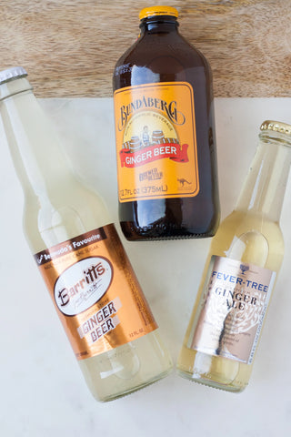 Three glass bottles lying on a table. Two are bottles of ginger beer, with the third being a bottle of ginger ale.