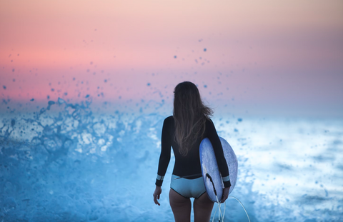 woman with surfboard entering the ocean waves