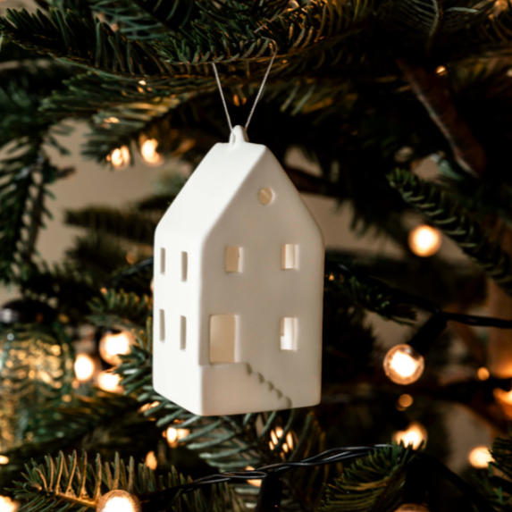 Porcelain house tree decoration hanging from Christmas tree with lights.