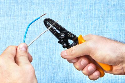 mains d'un homme coupant un fil électrique à l'aide d'une pince