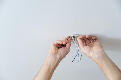 mains d'électricien qui réalise le branchement d'un plafonnier