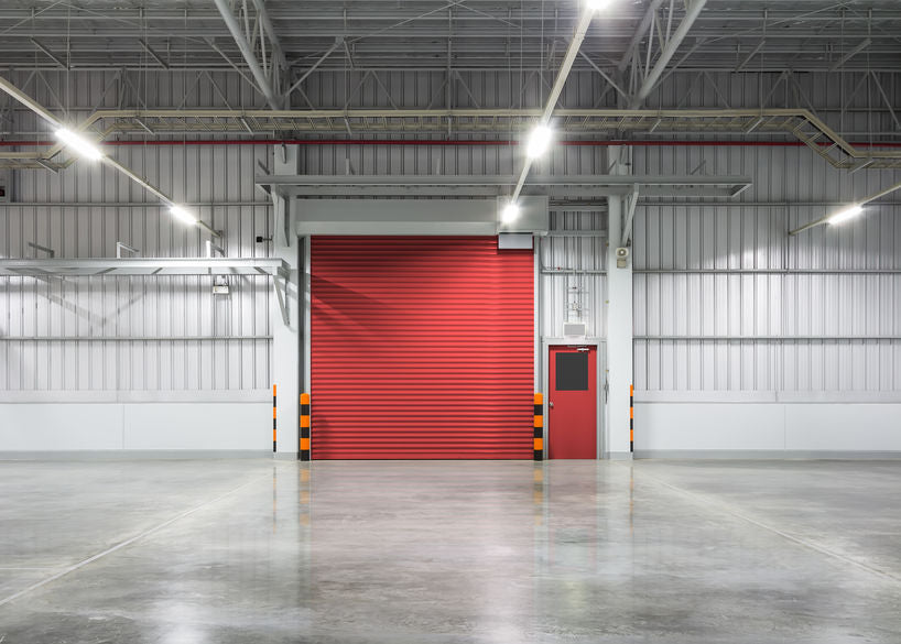 grand espace industriel vide éclairé par des néons LED, avec grande porte avec volet roulant rouge