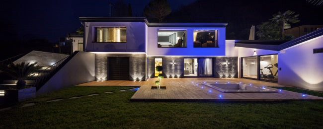 maison design éclairée de nuit par de multiples éclairages : spots sur la terrasse, bandes LED extérieures, etc.