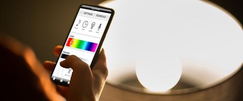 main qui tient un smartphone où est ouvert une applications connectée à une lampe led