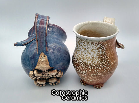 A purple cat butt mug and a soda fired cat butt mug.