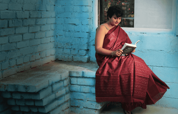 A female model in a seven saree silk collection reading a book. 