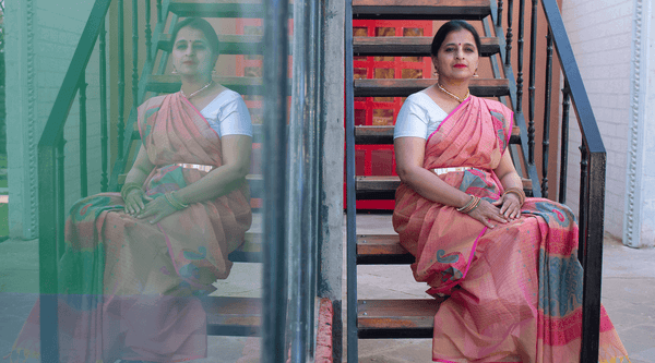 A female model in a colorful seven saree sitting next to a window with her reflection in the glass.. 