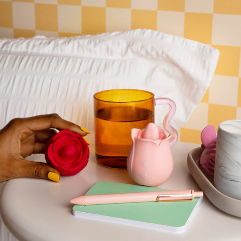 red and pink licking rose toy held in hand and on bedside table