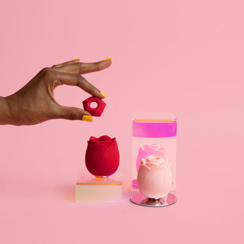 a hand holding a clit suction cap next to a pink rose toy