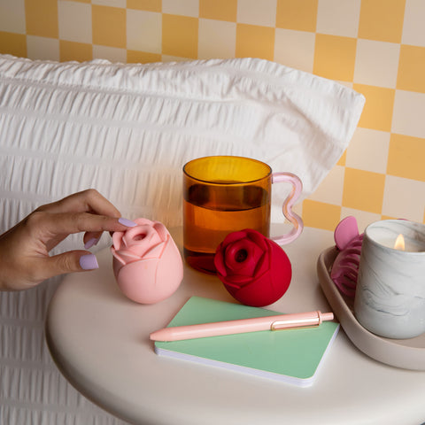 a hand touching the clitoral suction top of a pink pika rose toy  on a table