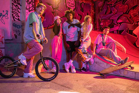 Group of five friends in streetwear fashion posing at skateboarding ground with bike and skateboard