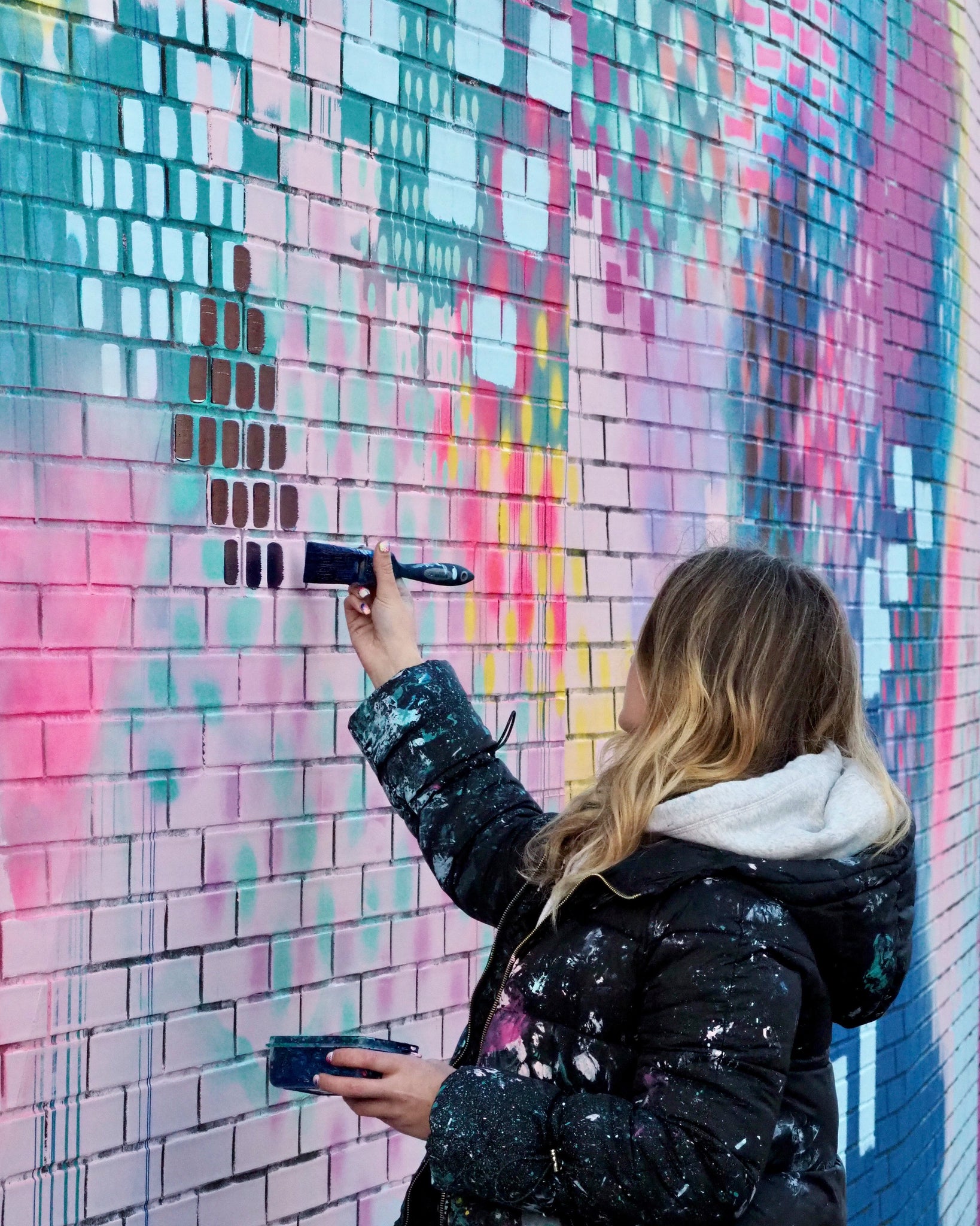 abstract artist painting brick wall with vibrant colours