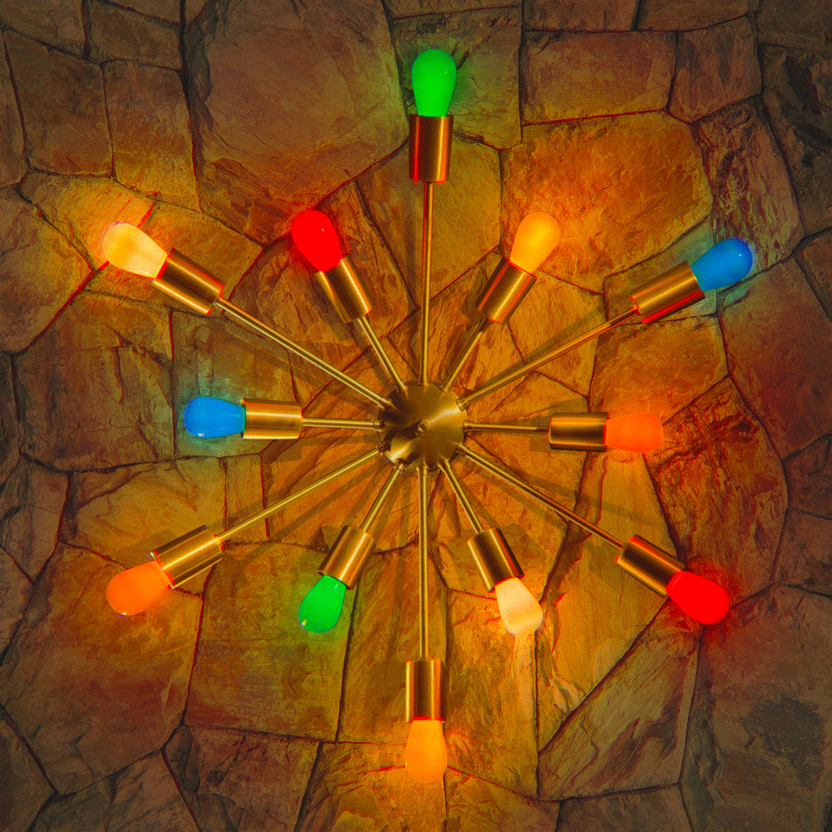 Colorful Tru-Tone S14 light bulbs in a mid-century Sputnik style brass light fixture on a stone wall
