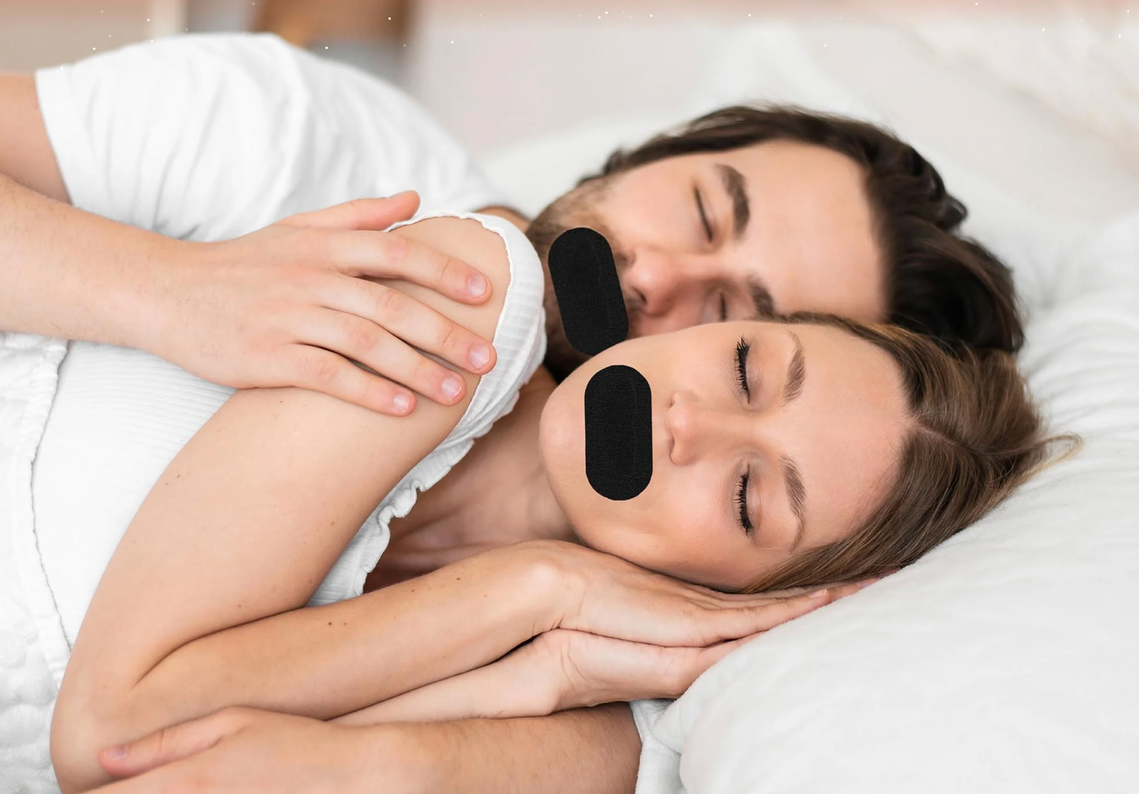 En mann og en kvinne sover tett med sort munntape på mens de ligger i en hvit seng
