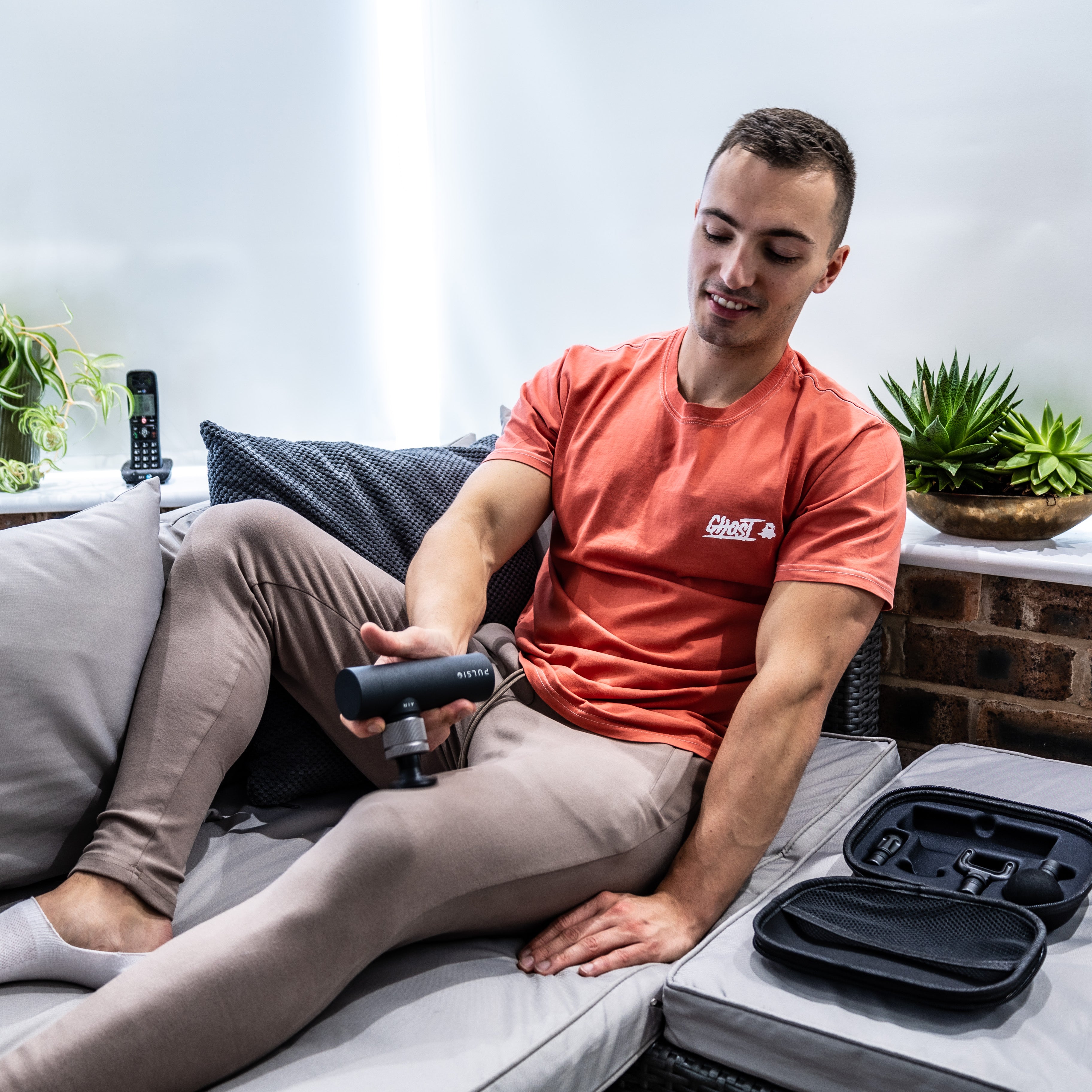 Man using a handheld massage device while sitting on a sofa.
