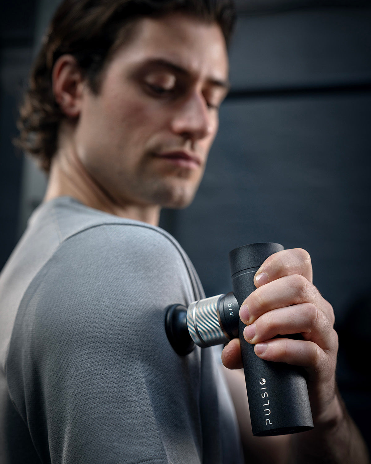 Man using a handheld massage device on his shoulder.