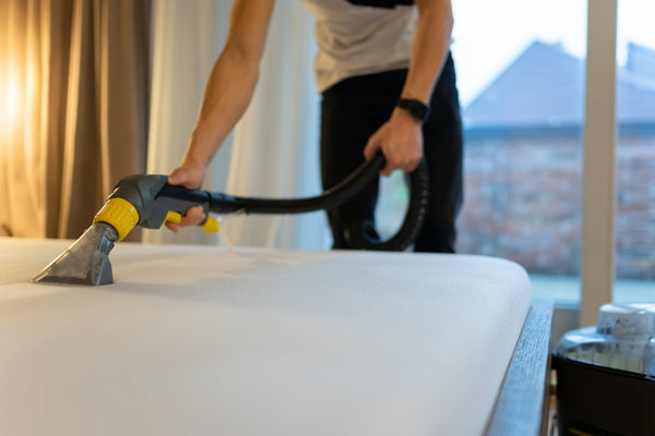 Image of a woman vacuuming a bed to remove dust and dirt. Keeping your bed clean is important for maintaining good hygiene and a healthy sleep environment