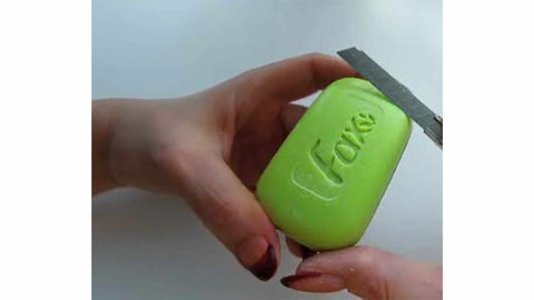 person cutting bar of green soap with box cutter