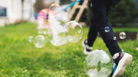 soap bubbles on lawn with child running behind them