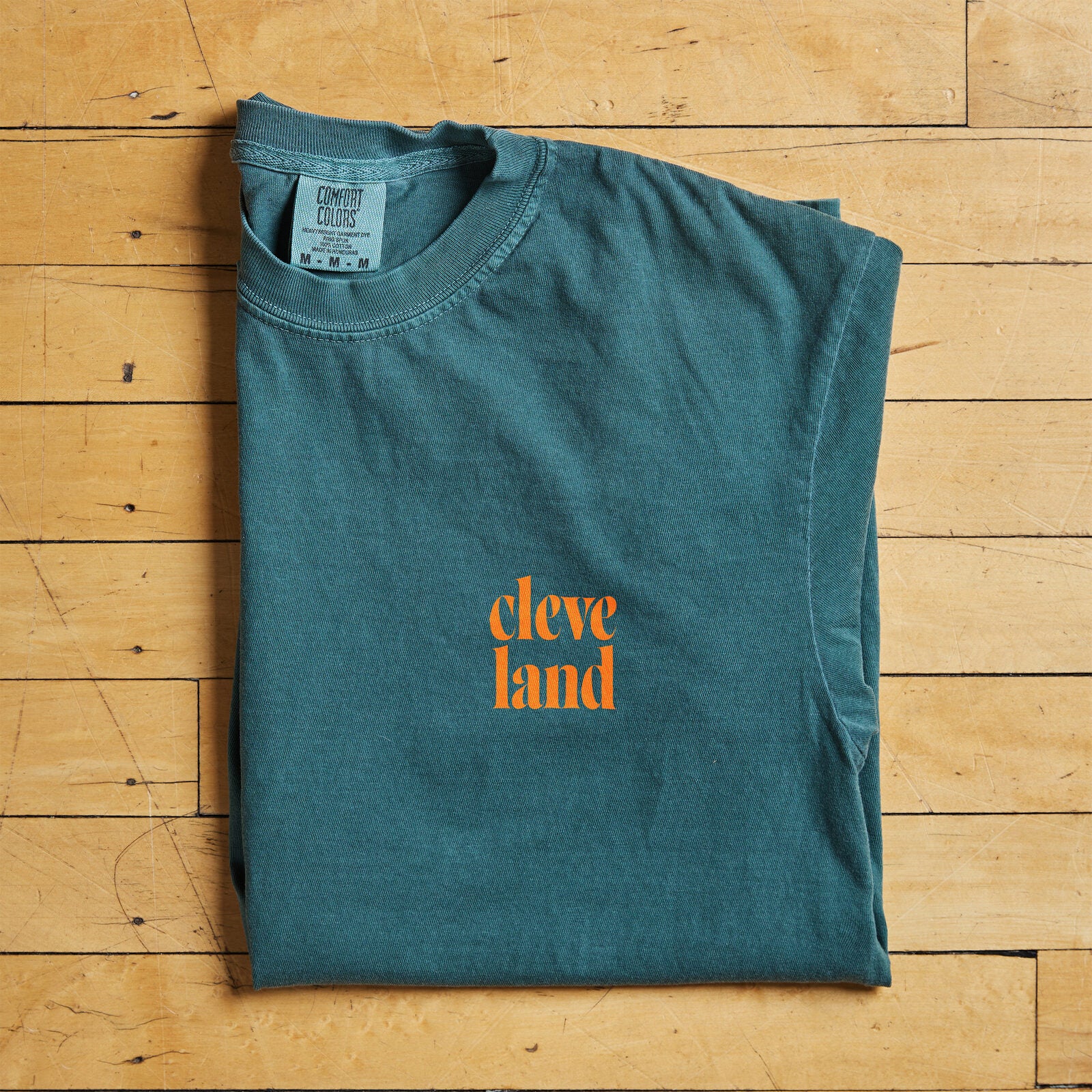 Cleveland t-shirt in teal with orange text folded flat on hardwood