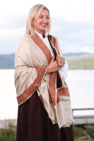 Sjalet Blomstereng er inspirert av norske skog og marker. Sjalet laget i fineste Kashmir ull som florlett og likevel varm og god. Sjalet kan brukes til både til hverdags og fest. Bildet viser sjalet i beig farge, kantet med broderier.