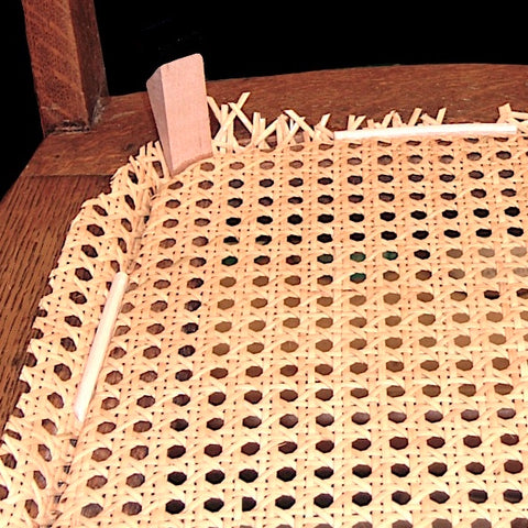 Installing pressed cane mesh into a seat using wooden wedges to hold it in place during installation