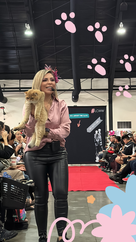 Person holding a purebred cat at a cat-themed event with people watching.