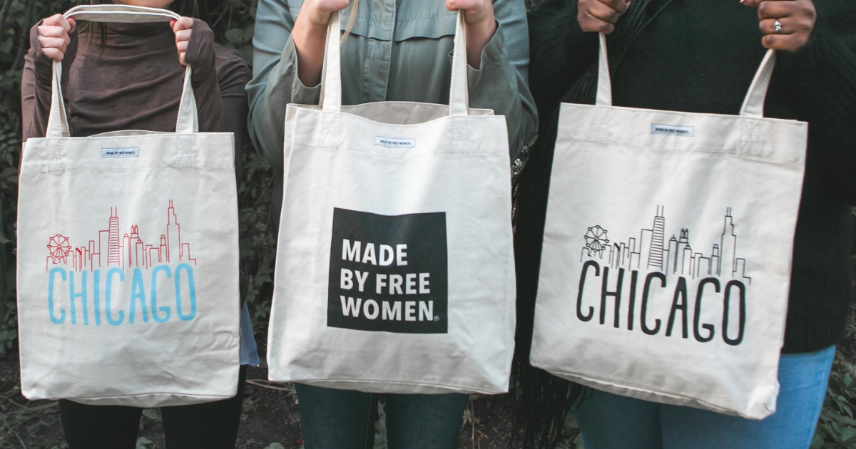 Three people stand side by side holding tote bags. The left tote bag says "CHICAGO" with a skyline graphic. The middle tote bag says "MADE BY FREE WOMEN." The right tote bag also says "CHICAGO" with a similar skyline graphic.