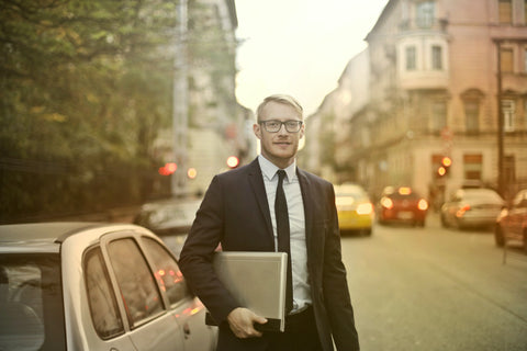 Image d'un homme d'affaire en costume tenant son calpin à côté de sa voiture