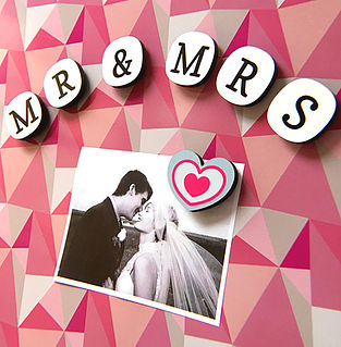 Letter fridge magnets spelling out Mr and Mrs on a pink geometric design magnetic board with a photo of a bride and groom attached with a heart shaped fridge magnet