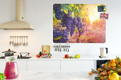 A kitchen interior with a counter top and a large magnetic board depicting a vineyard and sunset with postcards attached with fridge magnets