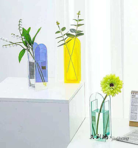 A group of 3 acrylic vases in soft pastel pink, blue and yellow hues arranged together on a wooden table.