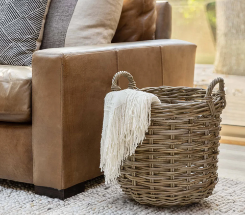 Kubu round storage tote basket with a blanket inside of it next to a couch.