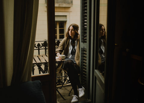 a woman sits with a coffee at a table on a small balcony in Europe