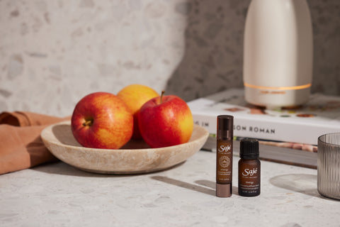 Energy roll-on and energy diffuser blend on a kitchen counter next to a bowl of apples and a stack of cookbooks