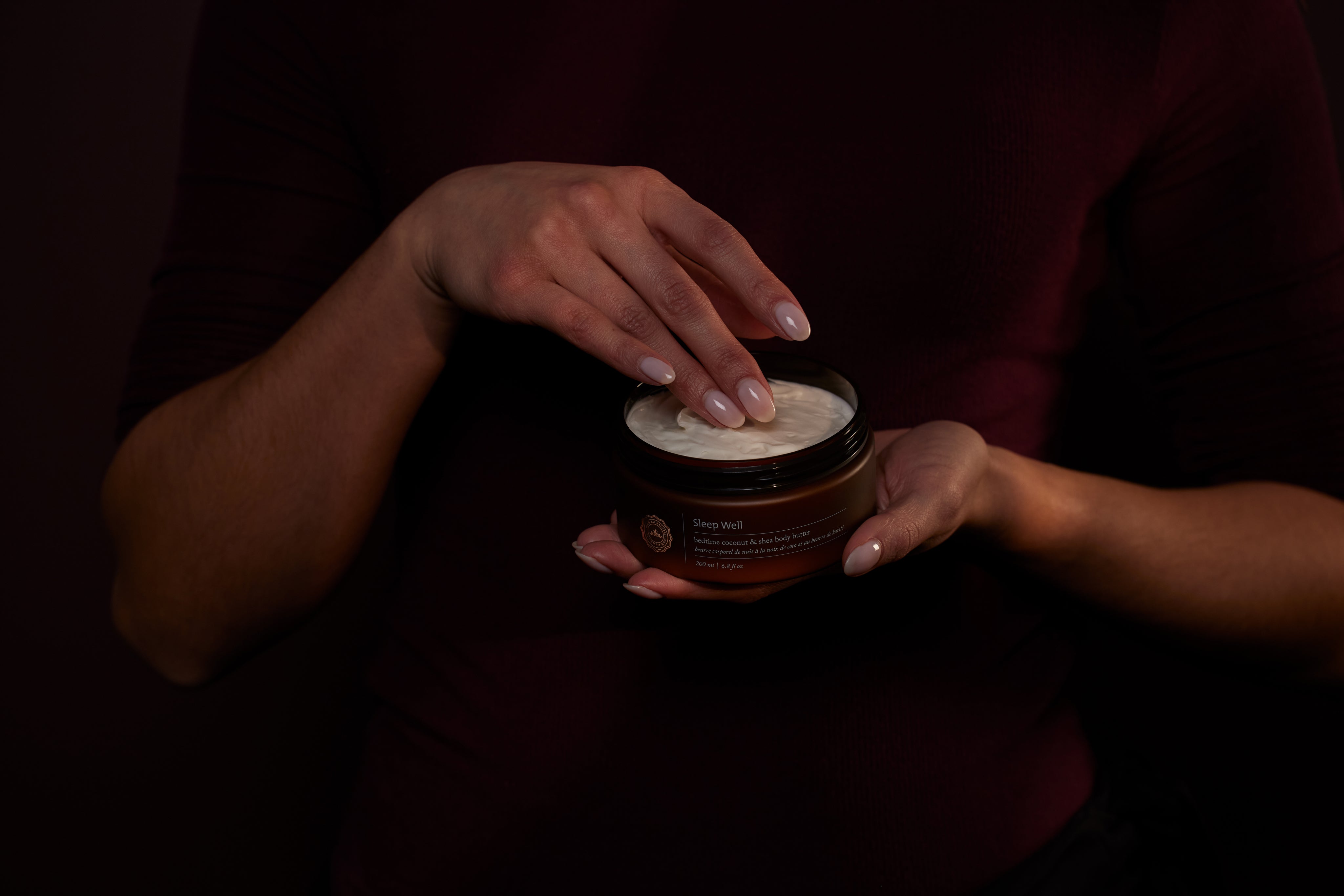 A person scooping sleep well body butter out of the container
