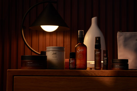 A collection of products from the Saje sleep line on a wooden nightstand against a dim lit background