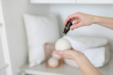 A person adding drops of a Saje diffuser blend to a dryer ball