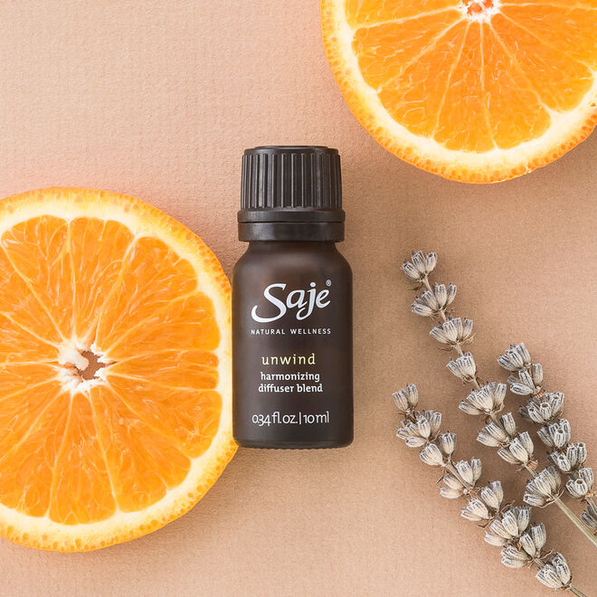 Unwind 0.34 fl oz diffuser blend bottle with cap on with orange slices and lavender sprigs behind it