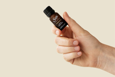 A hand holding a bottle of Tranquility diffuser blend against a beige background