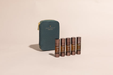Five Saje roll-ons lined up in front of a green Pocket Farmacy Mindful edition case against a cream background