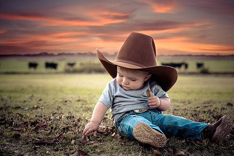 toddler boy in brown cowboy hat with cows in the background