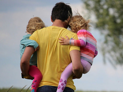 dad carrying his two daughters in a park
