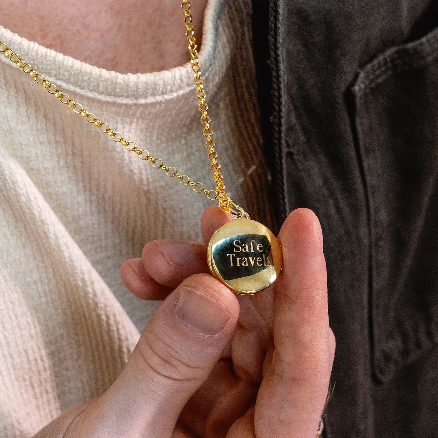 photograph of st christopher locket in gold showing the back of the locket with an engraved message "safe travels" worn on a male model